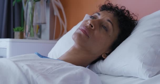 Seitenansicht einer Patientin mit gemischter Rasse, die im Krankenhausbett liegt, aufblickt und sich abwendet, Zeitlupe - Filmmaterial, Video