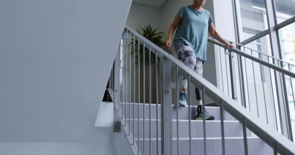 Front view of a Caucasian female patient with a prosthetic leg walking down a staircase at a hospital, for rehabilitation practice and exercise - Кадры, видео