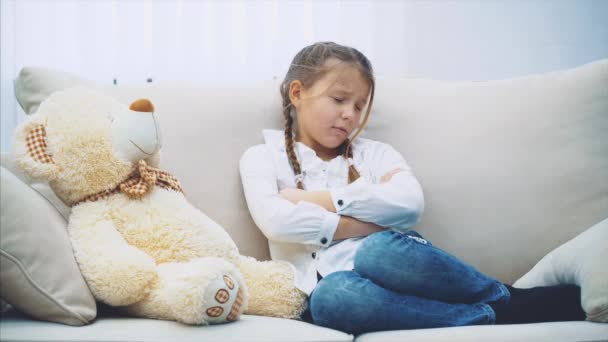 Schattig klein meisje op de bank, pratend met haar teddy, schaars uitleggend, wetend dat het haar niet begrijpt maar deze grote teddybeer knuffelend. - Video