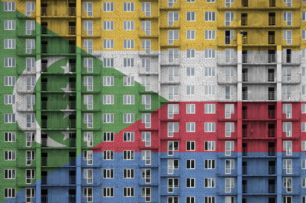 Komorská vlajka vyobrazená v barvách na vícepodlažní obytné budově ve výstavbě. Texturovaný banner na velké cihlové zdi pozadí - Fotografie, Obrázek