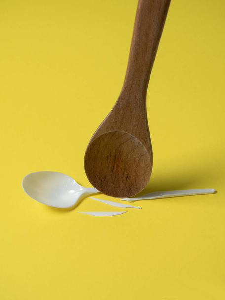 Wooden spoon breaks a plastic disposable spoon on a yellow background. Without plastic - Фото, изображение