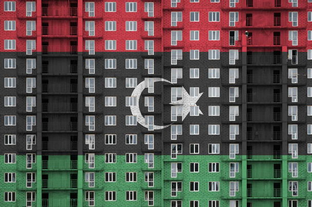 Bandera de Libia representada en colores de pintura en un edificio residencial de varios pisos en construcción. Banner texturizado sobre fondo de pared de ladrillo grande
 - Foto, imagen