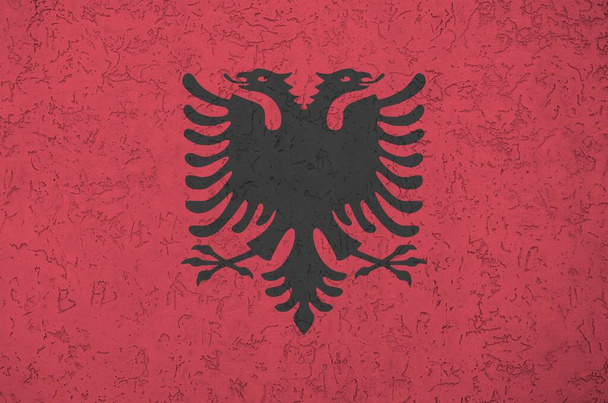 アルバニアの国旗は、古いレリーフの漆喰壁の上に明るい色で描かれている。ざらざらとした背景に書かれた旗 - 写真・画像