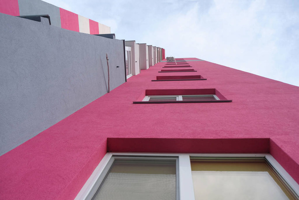 Nonstandard look. Shot from below. Pink with gray multistory house with new apartments. - Photo, Image