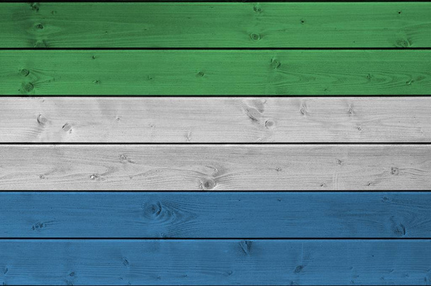 Флаг Сьерра-Леоне изображен в ярких красках на старой деревянной стене вблизи. Текстурированный баннер на грубом фоне
 - Фото, изображение