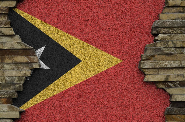 Timor Leste bayrağı eski taş duvardaki boya renkleriyle tasvir edilmiş. Kayalık duvar arkaplanındaki desenli pankart - Fotoğraf, Görsel