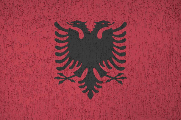 アルバニアの国旗は、古いレリーフの漆喰壁の上に明るい色で描かれている。ざらざらとした背景に書かれた旗 - 写真・画像