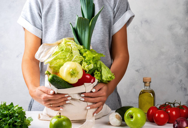 Женщина держит на кухонном столе экологически чистый мешок со свежими овощами. Концепция нулевых отходов
. - Фото, изображение