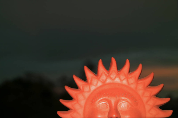 Closed up terracotta sun shaped home decor item against twilight dark blue sky - Photo, Image