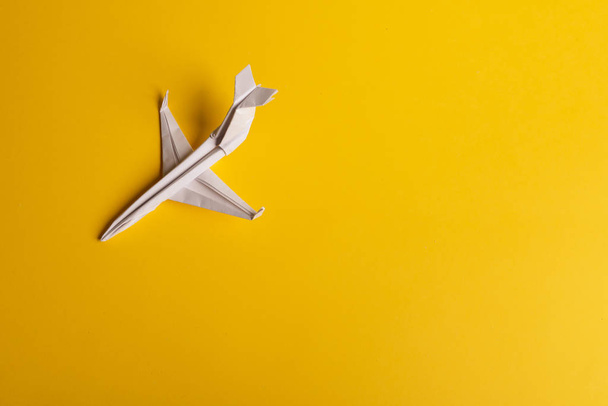 Ομάδα χάρτινων αεροπλάνων προς μία κατεύθυνση και με ένα άτομο να δείχνει με διαφορετικό τρόπο σε κίτρινο φόντο. Αιωρούμενη γραμμή από ουρά αεροσκάφους. - Φωτογραφία, εικόνα