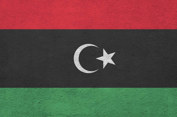 Eine libysche Flagge in hellen Farben auf alten Reliefputzwänden in Großaufnahme. Texturiertes Banner auf rauem Hintergrund - Foto, Bild