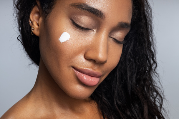 Rilassato afro americano donna sta applicando crema per il viso
 - Foto, immagini