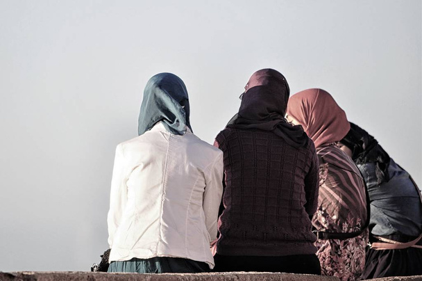 Group of women with colorful hijabs sitting on a bench and talking under a grey sky - Photo, Image