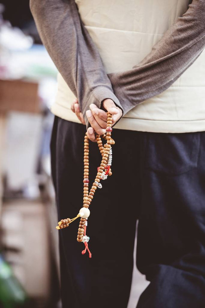 Vertical closeup shot of a male holding a chain of beads behind the back - Zdjęcie, obraz