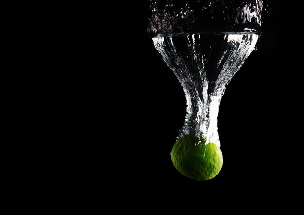 Closeup shot of a fruit thrown in the water with a black background - Фото, зображення