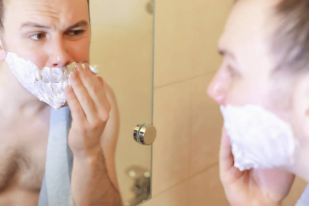 Ένας άντρας ξυρίζεται στο μπάνιο το πρωί. - Φωτογραφία, εικόνα