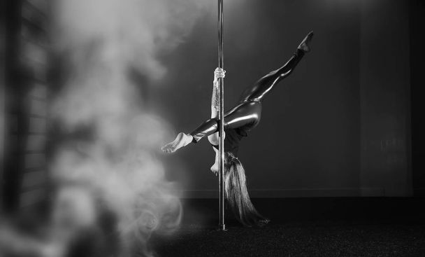 Girl doing exercises on a sports equipment. The dancer on the pylon in the studio. - Foto, immagini
