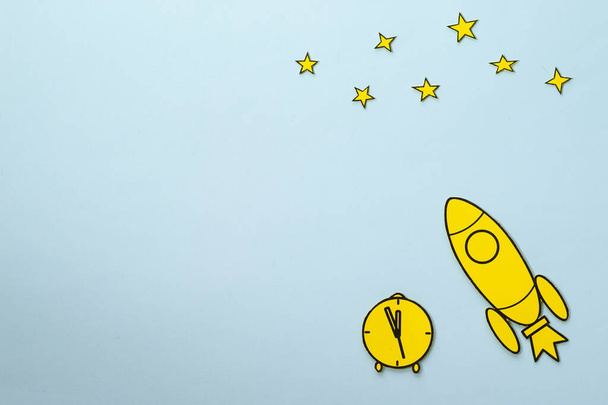 Gele kartonnen raket met klok en sterren op blauw - Foto, afbeelding