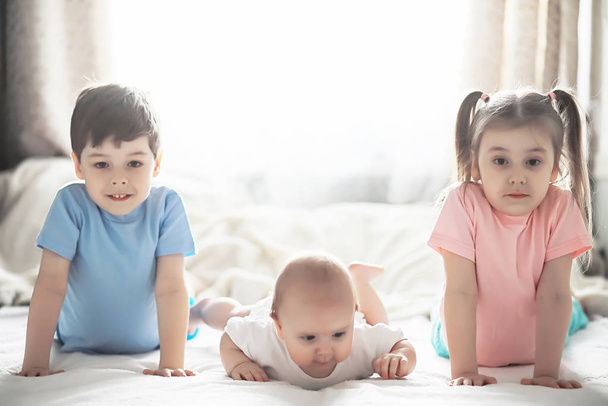 Children lie on the bed next to the newborn baby, little sister. - Valokuva, kuva