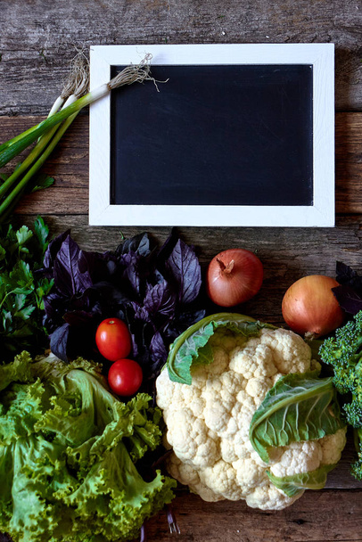 Verse groenten en kruiden op een oud ruw houten oppervlak en krijtbord voor inscriptie of menu, gezond eten concept, selectieve focus - Foto, afbeelding