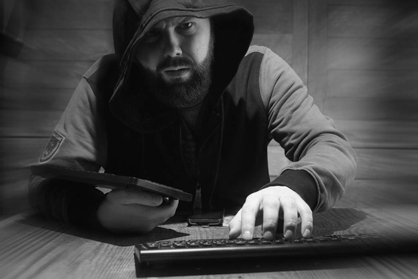 The hacker in the hood sits and works behind the computer - Foto, Imagen