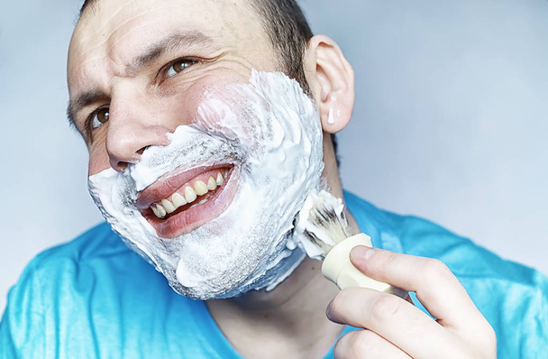 A man shaves in front a mirror. Shaving foam. Disposable razor. - Photo, Image