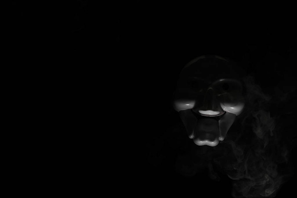 White scary mask on a black background with whites hand. - Photo, Image