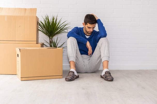 young man with mobile phone and moving boxes in the apartment - 写真・画像