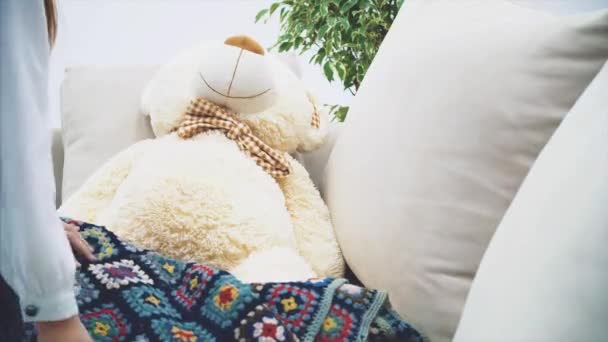 Beautful small kid covering teddy bear with a blanket, sitting near it, and reading a fairy-tale. - Felvétel, videó