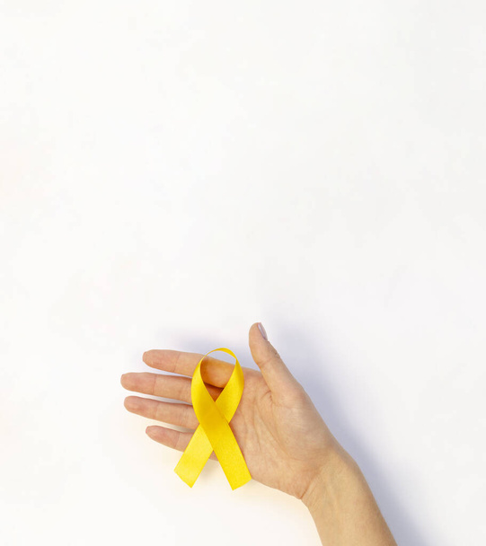 White vertical mockup poster Female hand holding Childhood Cancer Awareness Yellow Ribbon on white background. Top view Childhood Cancer Day concept on February, 15 - Photo, Image