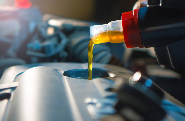Engine oil change. Fresh engine oil pouring from the canister into the automobile engine. Proper car care background. - 写真・画像