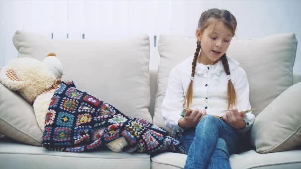 Pretty little girl reading fairy-tale for her teddy-bear, petting it, saing good-night. - Imágenes, Vídeo