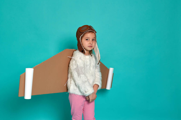 Маленька дівчинка грає з іграшковими крилами на синьому фоні. Щаслива дитина в костюмі космонавта грає і мріє стати астронавтом. Портрет дитини
. - Фото, зображення