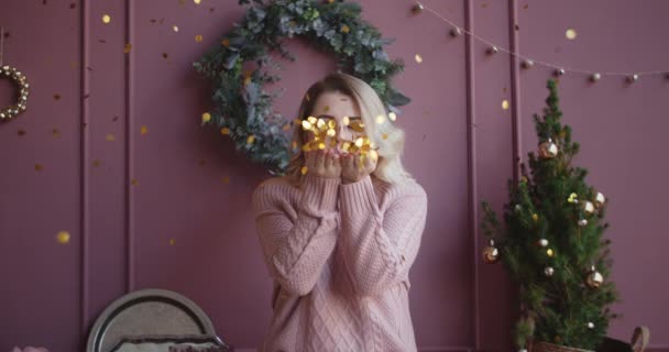 Mooie vrouw in trui blaast glimmende confetti van haar handen naar de camera in slow motion, kerst sfeer, vallende gouden confetti, oudejaarsavond, kerst selebration, 4k Dci 120fps Prores Hq - Video