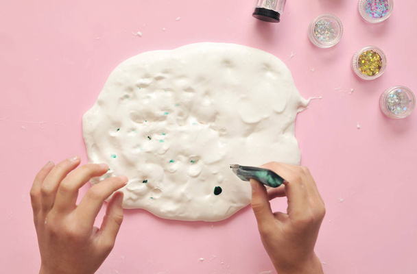 Child hands with home-made slime. Baby makes slime with glue and glitters on pink background. - Φωτογραφία, εικόνα