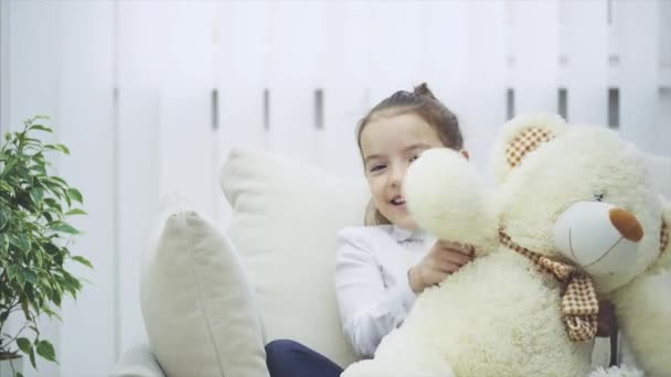 Child and teddy on the sofa. Gorgeous girl is playing with her soft friend. - Video