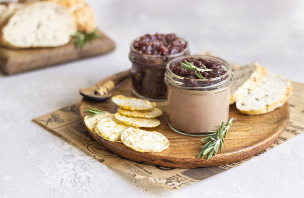 Fresh homemade chicken liver pate and onion chutney (marmalade) in a jar, bread and crackers on a wooden plate. Light grey background, selective focus. - Фото, изображение