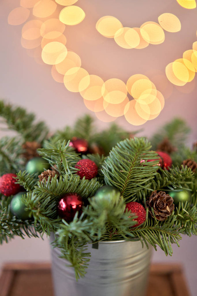 Small arrangement of fresh spruce in a metal pot. Christmas mood. Bokeh of Garland lights on background. - Photo, Image