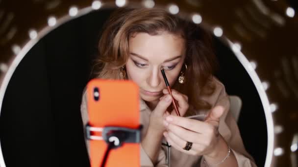 Caucásico mujer maquillaje artista se aplica sombra de ojos sentado en frente de la luz del anillo
 - Imágenes, Vídeo