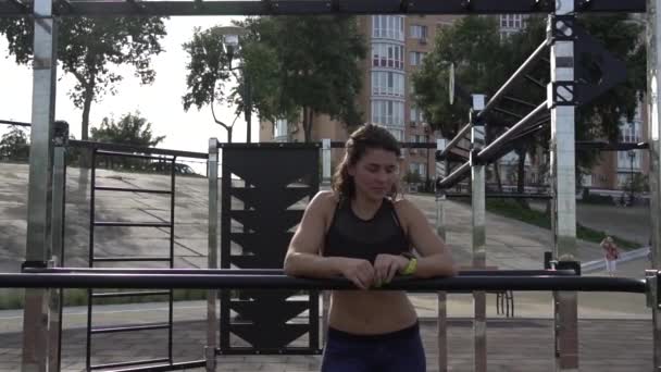 Attractive fit young woman in sport wear rest on the street workout area. The healthy lifestyle in the city. Street portrait strong woman poses at gym. Beautiful athletic woman in sports bra posing - Footage, Video