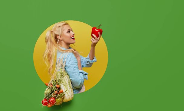 Genç bir kadın yeşil arka planda bir ip torbasında taze sebzeler topladı. Duvardaki yuvarlak delikten dışarı bakıyor. Retro ve pin stili. Düzgün beslenme ve vejetaryenlik kavramı. - Fotoğraf, Görsel