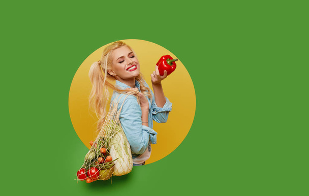 Молода жінка зібрала свіжі овочі в сумці на зеленому тлі. Виглядає з круглої діри в стіні. Ретро і стиль прищипування. Концепція правильного харчування та вегетаріанства
. - Фото, зображення