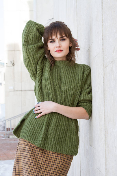młoda dziewczyna w zielonym swetrze stoi opierając się o marmurową ścianę - Zdjęcie, obraz