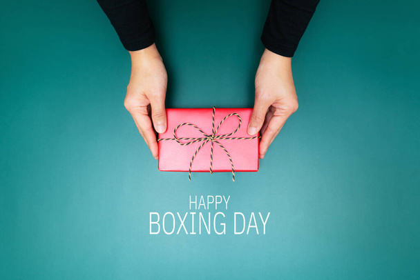 Χαρούμενη ημέρα πυγμαχίας, νεαρή γυναίκα χέρι με μια προσφορά κουτί δώρου στο δέκτη - Φωτογραφία, εικόνα