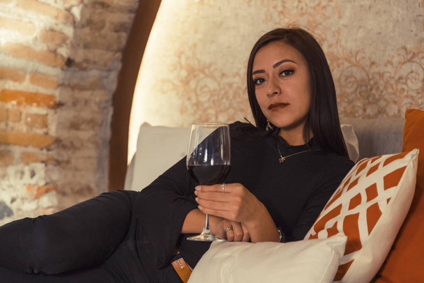 Retrato de uma jovem mulher de negócios latina séria com copo de vinho no quarto - Foto, Imagem