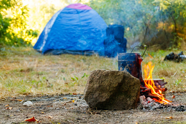 Cooking on campfire in camping. Tent and backpack on background - Photo, Image