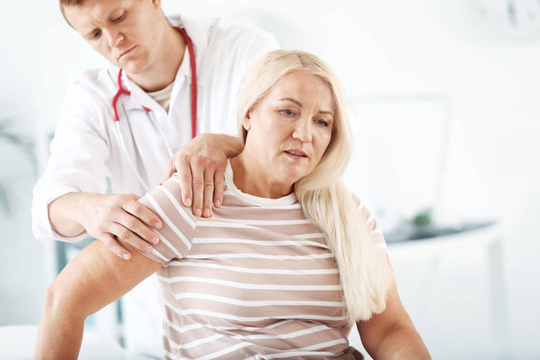 Médico examinando mujer madura con dolor articular en la clínica
 - Foto, imagen