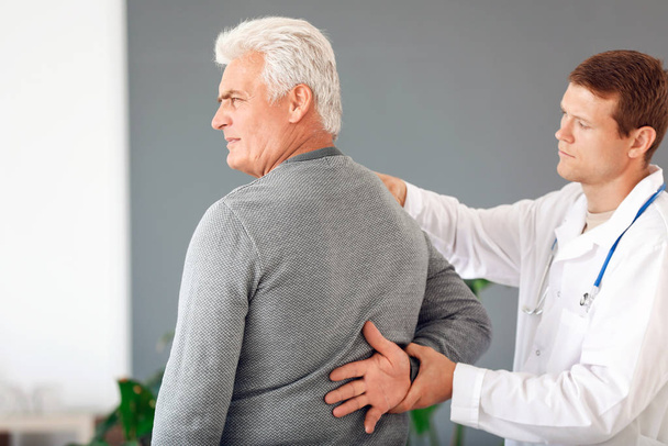 Doctor examining mature man with joint pain at home - Foto, imagen