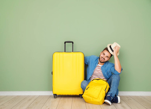 Joven turista masculino con equipaje sentado cerca de la pared de color
 - Foto, imagen