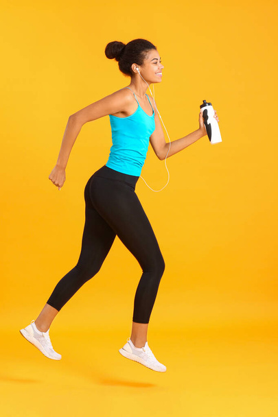 Laufen afrikanisch-amerikanische Frau mit Flasche Wasser auf farbigem Hintergrund - Foto, Bild
